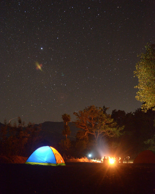 Glowing tent and campfire under a starry sky